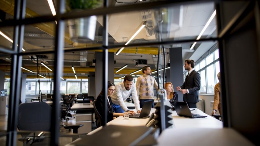 Team gathered around laptops at a shared desk in an open plan office