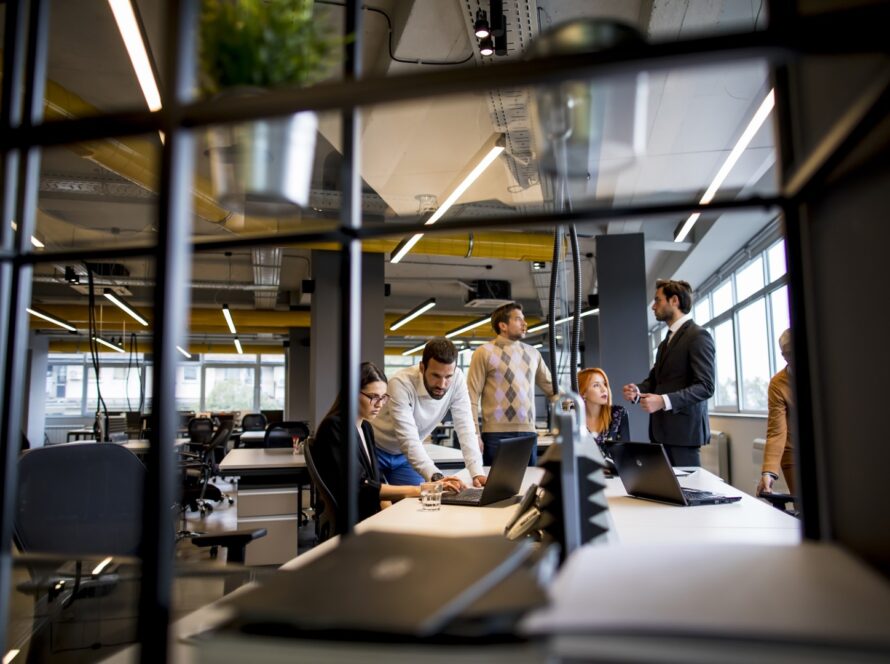 Team gathered around laptops at a shared desk in an open plan office